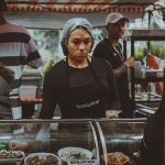 Vendedora de comida prepara pratos em uma movimentada feira de rua em São Paulo.