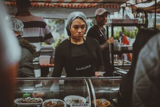 Vendedora de comida prepara pratos em uma movimentada feira de rua em São Paulo.