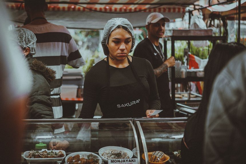 Vendedora de comida prepara pratos em uma movimentada feira de rua em São Paulo.