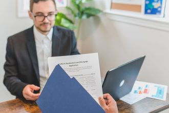 Corretor e cliente analisam uma solicitação de empréstimo e documentos sobre a mesa.