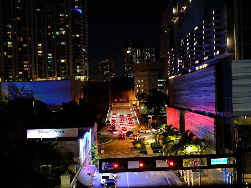 Vista noturna de Brickell, em Miami, com arranha-céus iluminados, trânsito e movimento urbano.
