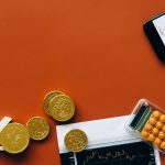 Moedas, calculadora e gráficos sobre uma superfície vermelha, representando análise financeira e indicadores econômicos.