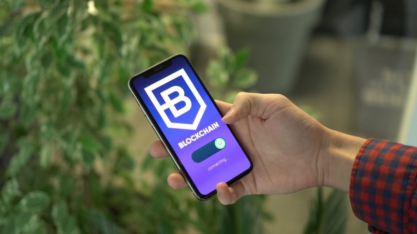 Mão segurando um smartphone com a tela de um aplicativo de blockchain.