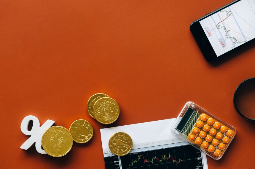Moedas, calculadora e gráficos sobre uma superfície vermelha, representando análise financeira e indicadores econômicos.